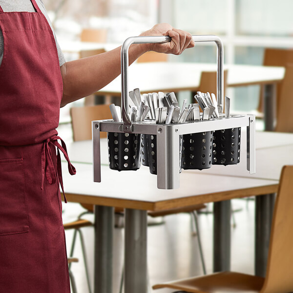 A man holding a metal flatware carrier with black stainless steel perforated cylinders filled with utensils.
