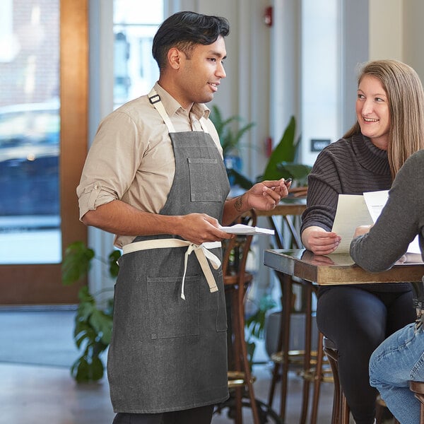 A man and woman in Acopa denim aprons talking to a woman at a table.