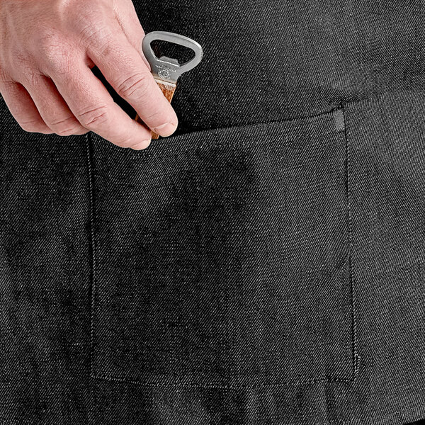 A person using an Acopa Kennett black denim half bistro apron with black webbing and pockets to open a bottle of wine.