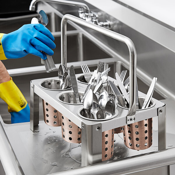 A person in gloves washing utensils in a metal rack on a counter.