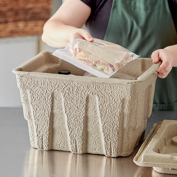 A person putting a sandwich in a Fiber Cooler Base container.