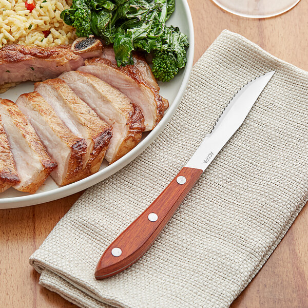 An Acopa steak knife next to a plate of meat and rice with vegetables.