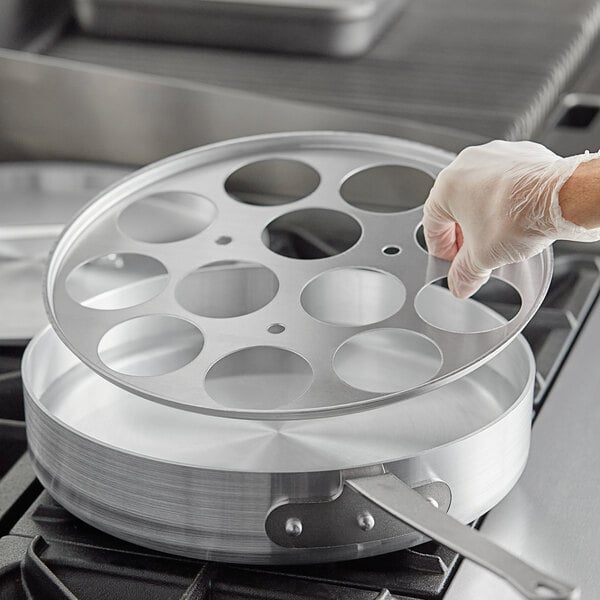 A person in white gloves using a Choice aluminum egg poacher inset on a stove.