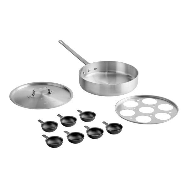 A stainless steel sauté pan with a long handle, a matching lid, a metal insert with seven circular cutouts, and seven small non-stick cups with handles arranged in front.