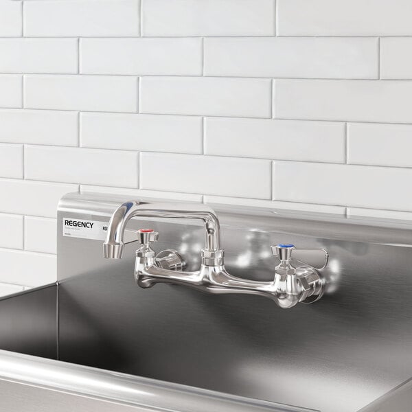 A stainless steel wall mount faucet with an 8-inch swing spout and dual handles, installed above a commercial sink.