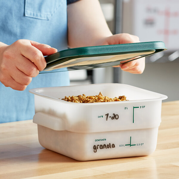 A person holding a white Vigor food storage container filled with food and covered with a green lid.