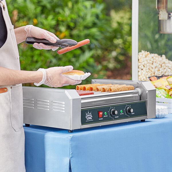 A person using a Carnival King hot dog roller grill to cook hot dogs.