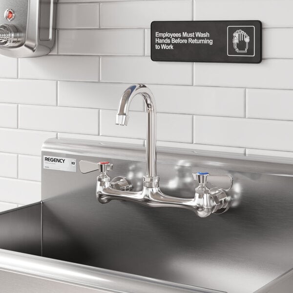 A stainless steel wall mount faucet with a 3 1/2-inch swivel gooseneck spout and dual handles, installed on a commercial sink.