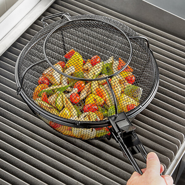 A person using the Outset grill basket to cook vegetables on a grill.