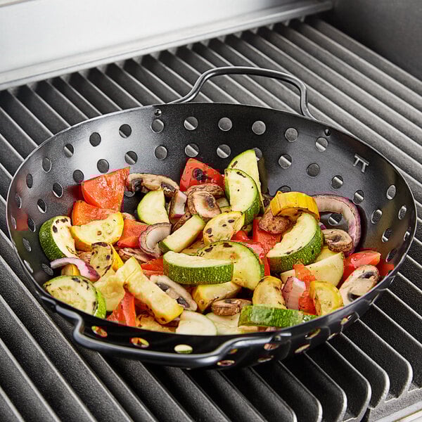 An Outset non-stick grill basket with vegetables on a grill.