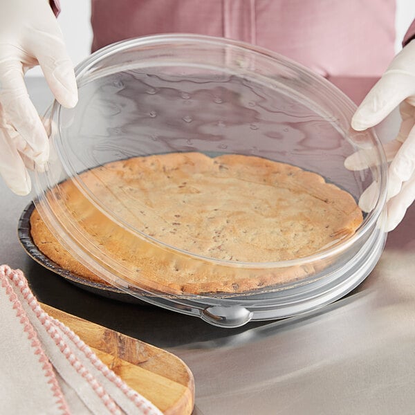 A gloved hand holding a pie in a clear plastic container.