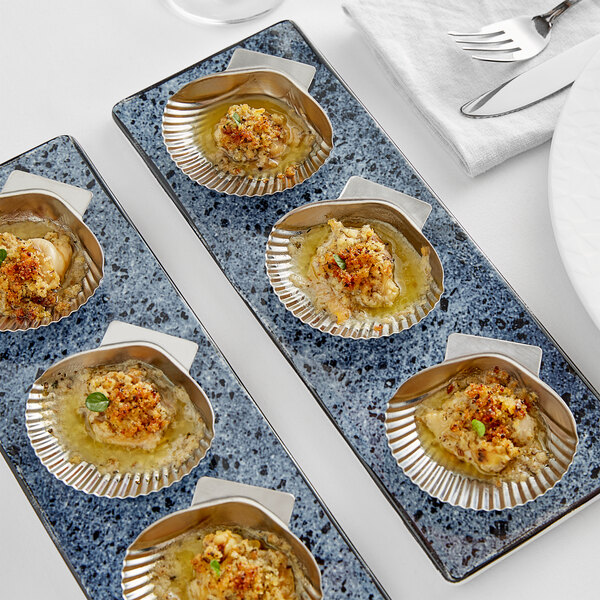 A tray of stainless steel clam grill shells on a table.