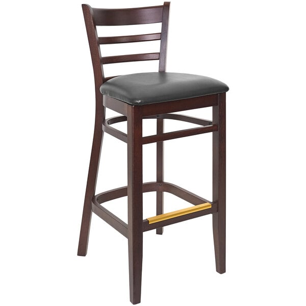A BFM Seating Berkeley dark walnut beechwood ladder back barstool with a black vinyl seat.