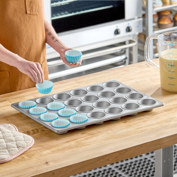 A 24-cup glazed aluminized steel muffin or cupcake pan on a wooden countertop.