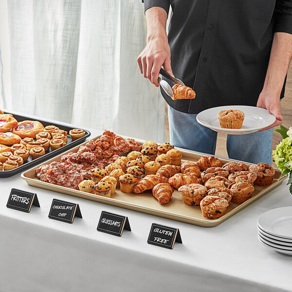 A man serving pastries on a Baker's Mark gold wire rim sheet pan on a hotel buffet table.