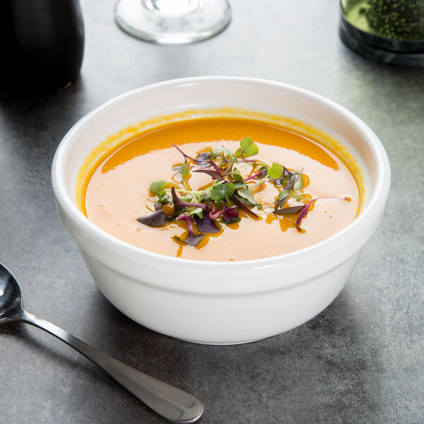 A white Tuxton china bowl of soup with a spoon.