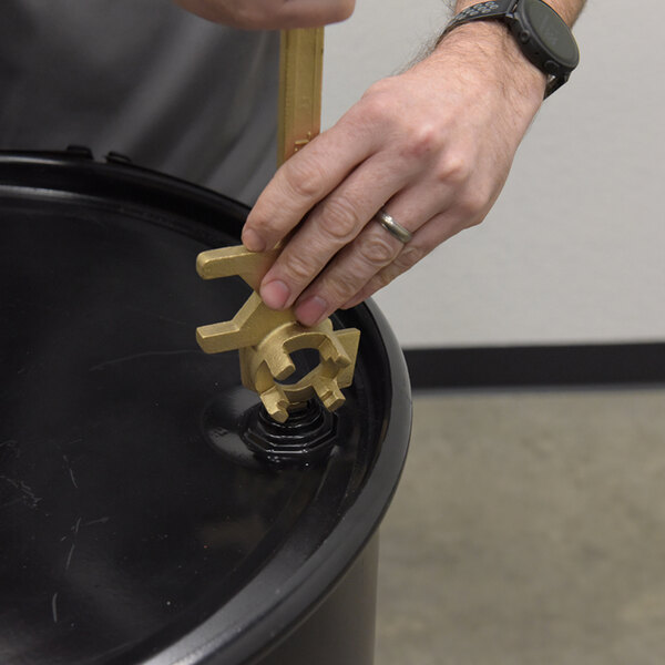 A non-sparking bronze alloy drum bung nut wrench being used to open a black drum lid.
