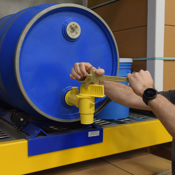 A non-sparking bronze alloy drum bung nut wrench with a faucet wrench being used on a blue drum with a yellow spigot.