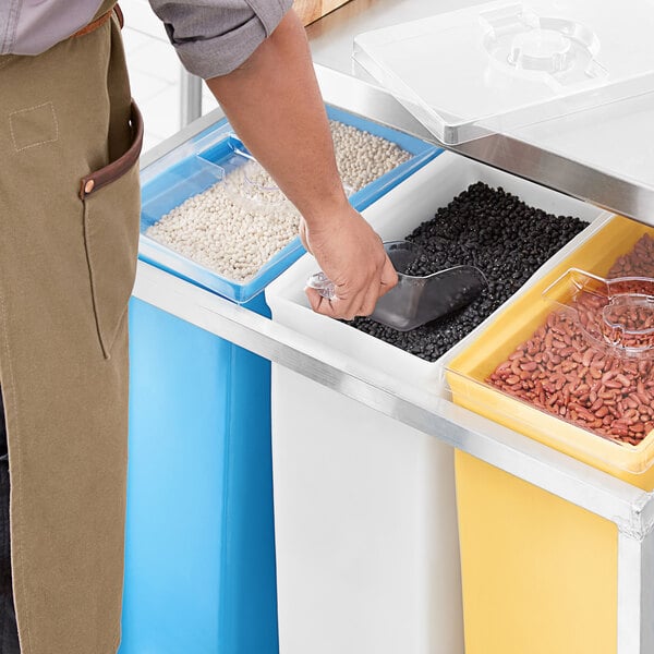 A person using a scoop to put black beans into a Channel white ingredient container.