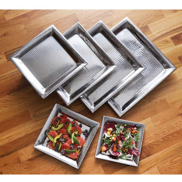 A group of silver trays with salad and vegetables on them.