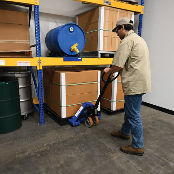 A person pushing a Vestil hand pallet truck with a pallet.