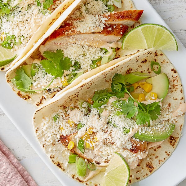 A plate of tacos with V&V Supremo Cotija cheese crumbles, vegetables, and limes.