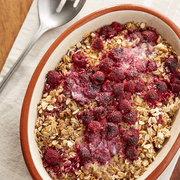 A bowl of oatmeal with raspberries and a spoon.