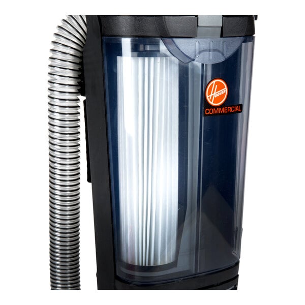 A close-up view of a vacuum cleaner's dust canister with a visible pleated filter and a flexible hose attached.
