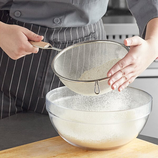 A person using a Vollrath fine mesh strainer to sift powder into a bowl.
