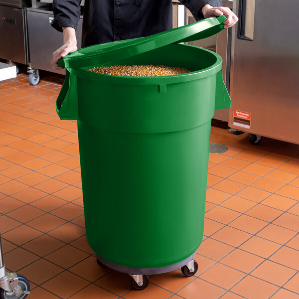 A man in a chef's uniform holding a green Mobile Ingredient Storage Bin full of food.