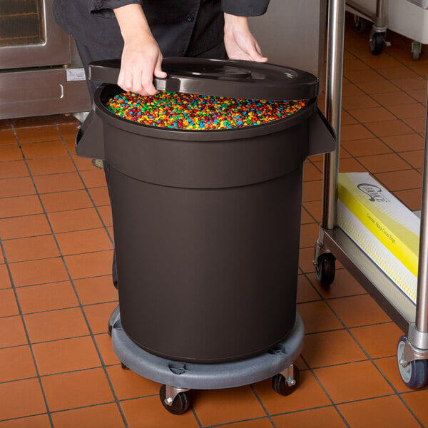 A woman putting colorful candies into a brown mobile ingredient storage bin with lid.