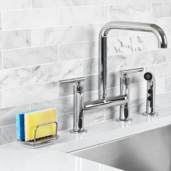 A stainless steel OXO sponge holder on a kitchen sink counter.