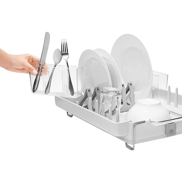 A hand holding a knife and fork in a white OXO dish drying rack.