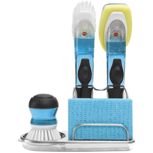 An OXO Good Grips sink organizer holding a blue and white dish brush.