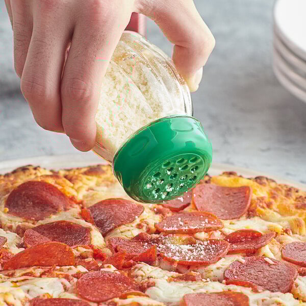 A person pours cheese from a Tablecraft clear plastic swirl shaker with a green perforated top onto a pizza.