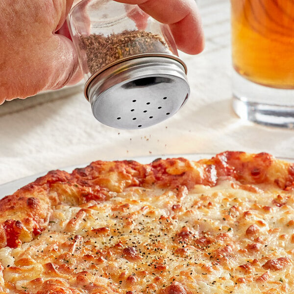 a hand holding a pepper shaker over a pizza