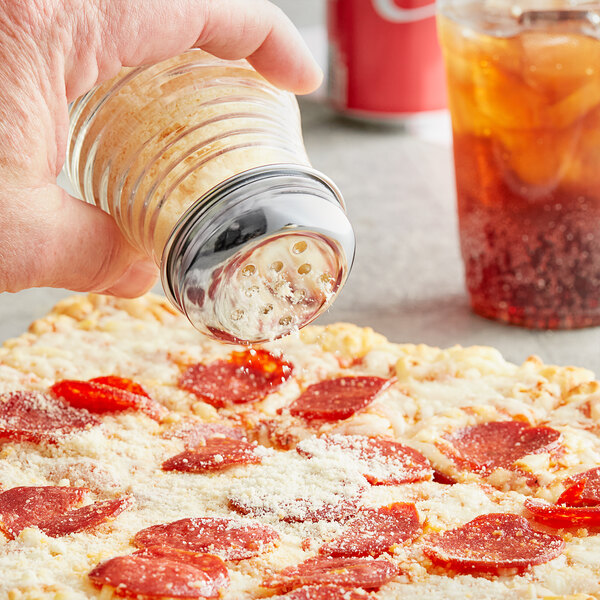 A person using a Tablecraft glass cheese shaker to sprinkle cheese on a pizza.