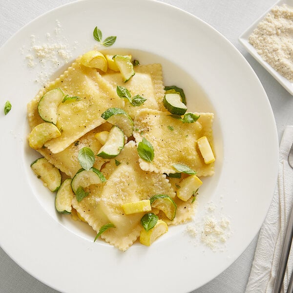 A plate of ravioli pasta served with sliced zucchini, yellow squash, fresh herbs, and a sprinkle of cheese seasoning.