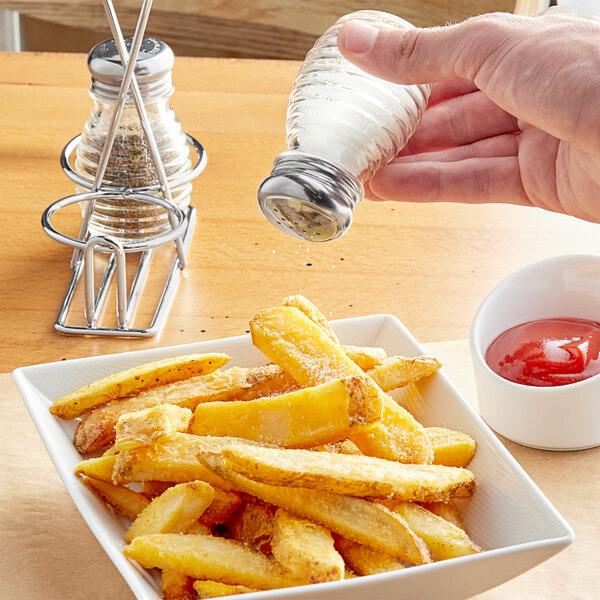 A person using a Tablecraft beehive salt shaker to pour salt on french fries.