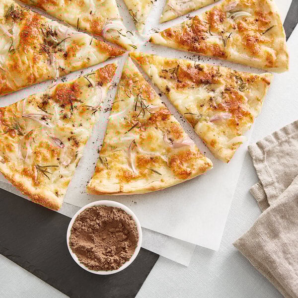 A sliced white pizza topped with cheese, onions, herbs, and a small bowl of truffle zest seasoning on the side.