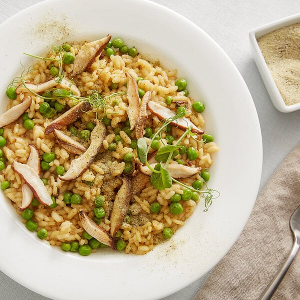 A bowl of risotto with green peas and sliced mushrooms, garnished with herbs and a sprinkle of truffle and rosemary sea salt.