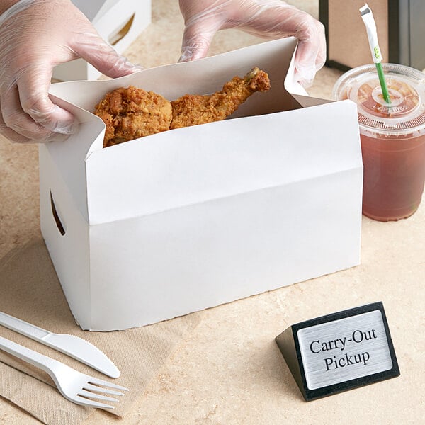 A person putting chicken in a white take-out box.