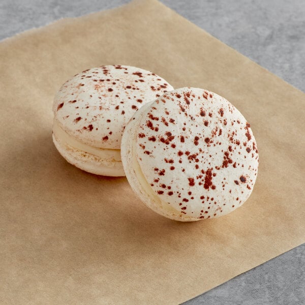 Two white and chocolate Macaron Centrale macarons on brown paper.