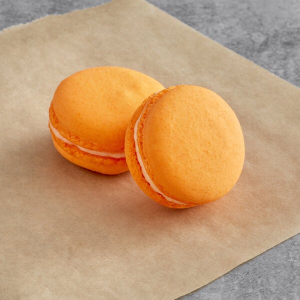 Two orange Macaron Centrale cookies with white filling on brown paper.