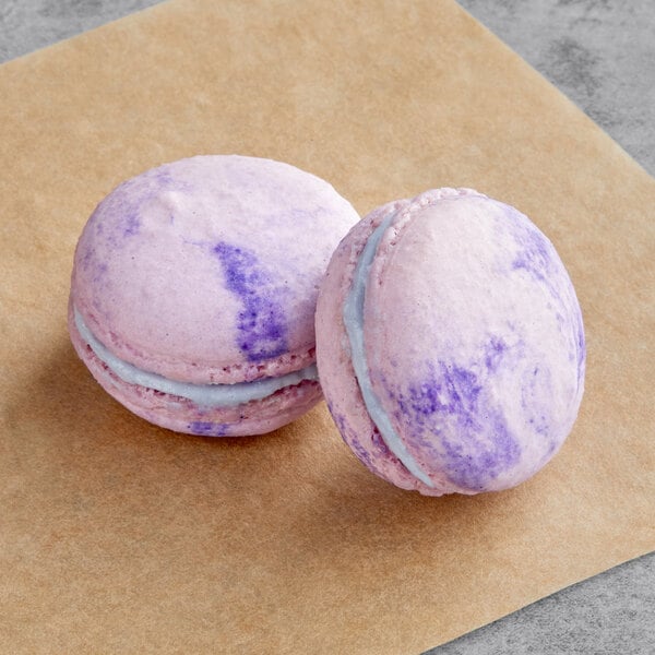 Two purple and white Macaron Centrale butterfly pea flower macarons on a brown paper.