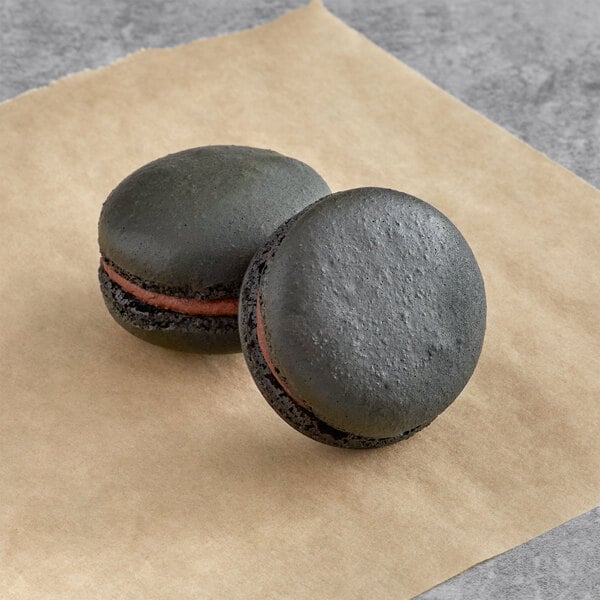 Two black Macaron Centrale espresso macarons on brown paper on a counter.