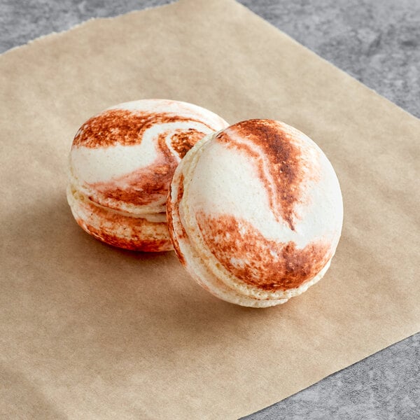 Two Macarons with brown and white icing on paper.