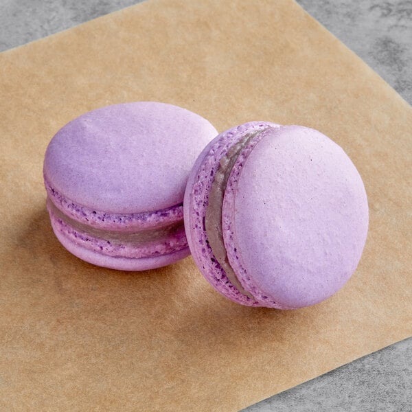 Two grape macarons on a brown surface.