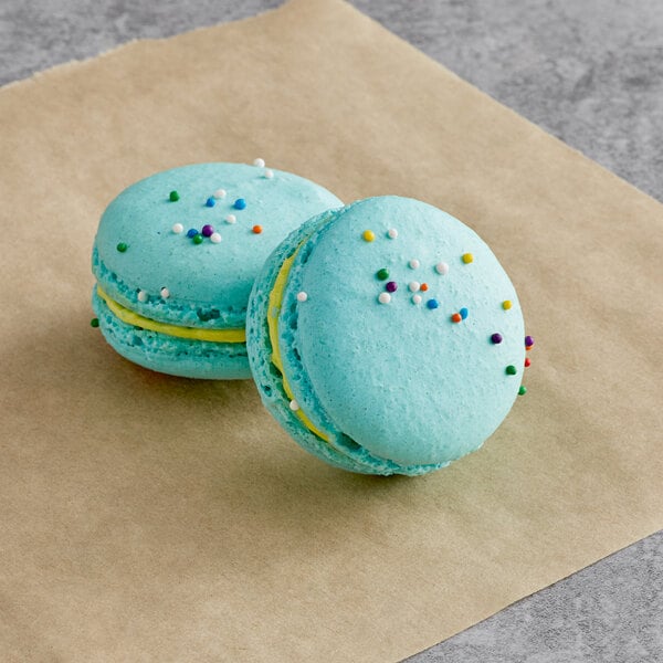 Two blue Macaron Centrale macarons with sprinkles on a brown surface.