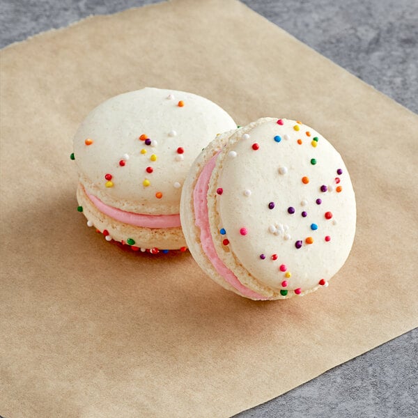 Two Macaron Centrale birthday macarons with white cookies and sprinkles.